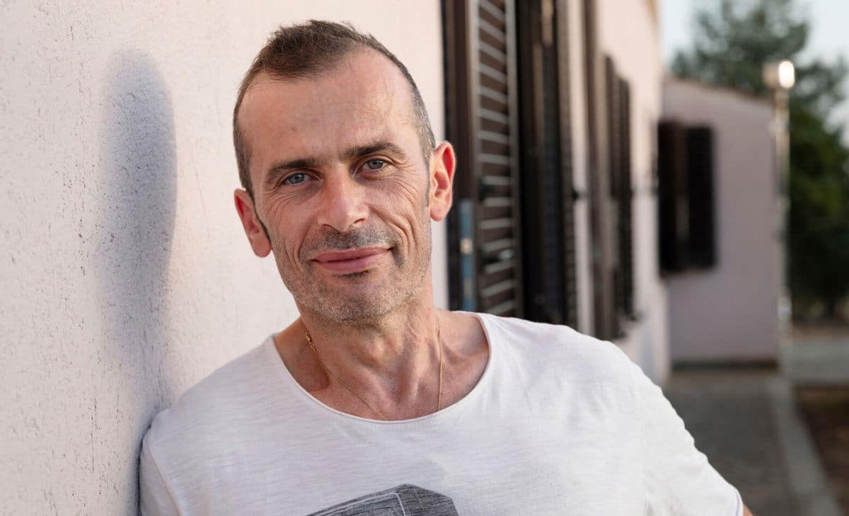 Foto di Andrea davanti alla sua casa. Andrea convive con la SM e avrebbe voluto sapere qualcosa in più su cosa aspettarsi riguardo ai problemi alla vescica e all'intestino.  