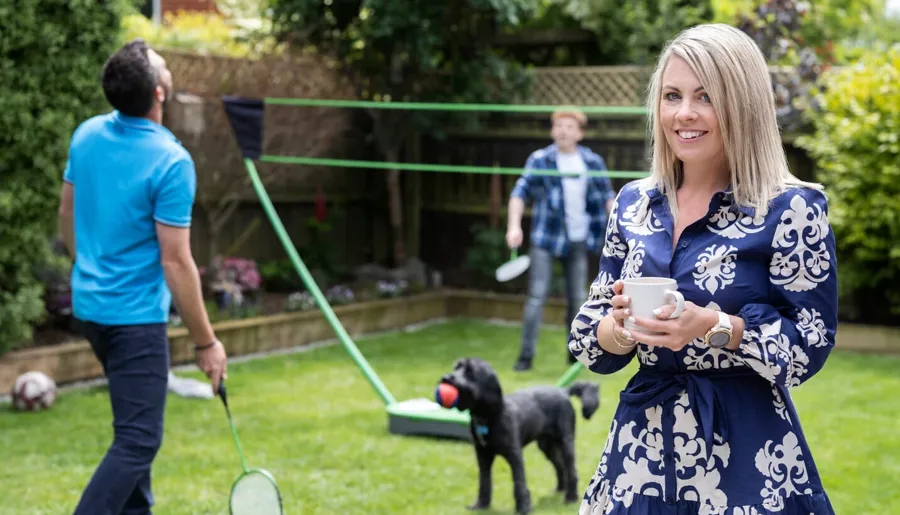 Laura è nel suo giardino con la famiglia che gioca sullo sfondo. Laura pratica la TAI per gestire i problemi intestinali causati dalla sclerosi multipla.